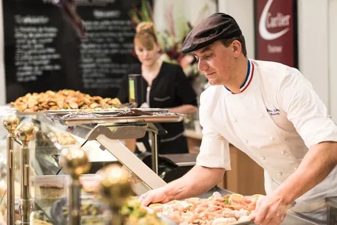 charcutier-traiteur coiffé d'une toque arrange des préparations froides en vitrine