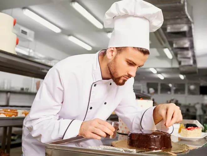 pâtissier en toque décorant un entremet au chocolat dans une cuisine professionnelle