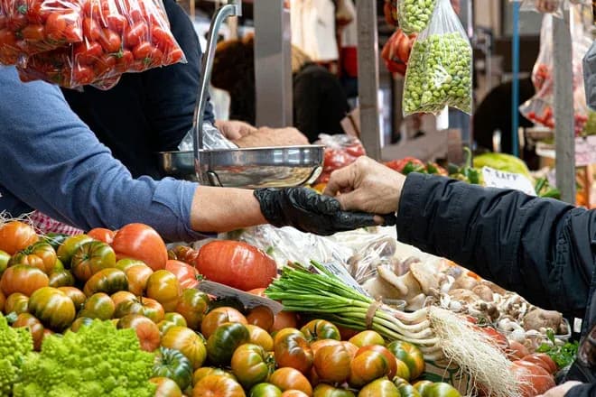 mains d'un vendeur et d'un client échangeant de l'argent devant un étal de légumes