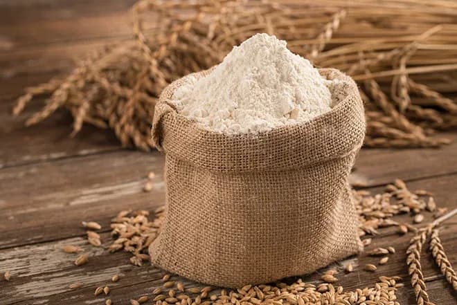 sac en toile rempli de farine posé sur planche avec épis et grains de blé