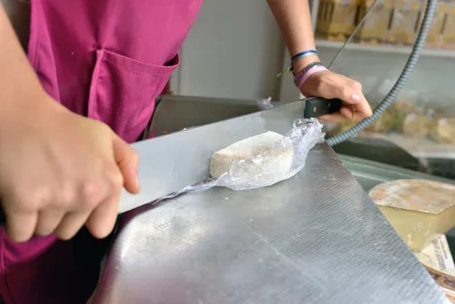 mains tenant un couteau professionnel tranchant un petit fromage emballé sur plan métallique