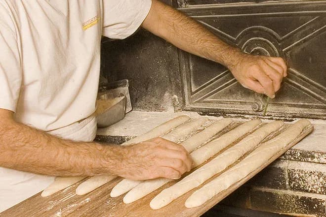 mains d'un boulanger incisant des baguettes sur une pelle avant cuisson