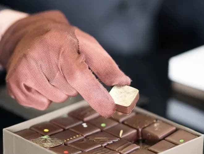main d'un chocolatier portant des gants en train de sélectionner un chocolat dans une boîte