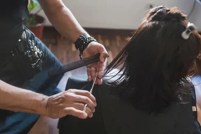 coiffeur coupant les cheveux d'une cliente avec des ciseaux et un peigne dans un salon