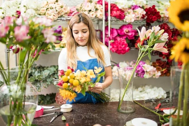 jeune femme préparant un bouquet dans une boutique avec étagères de fleurs
