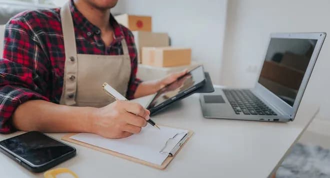 commerçant en tablier saisissant des informations de colis sur tablette et carnet