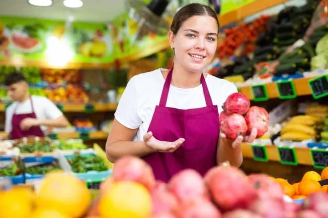 jeune vendeuse primeur présentant des grenades au rayon fruits