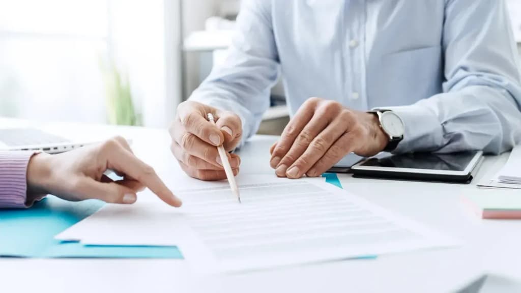 Mains de deux personnes penchées sur des documents lors d'une consultation, un crayon et une tablette sur le bureau