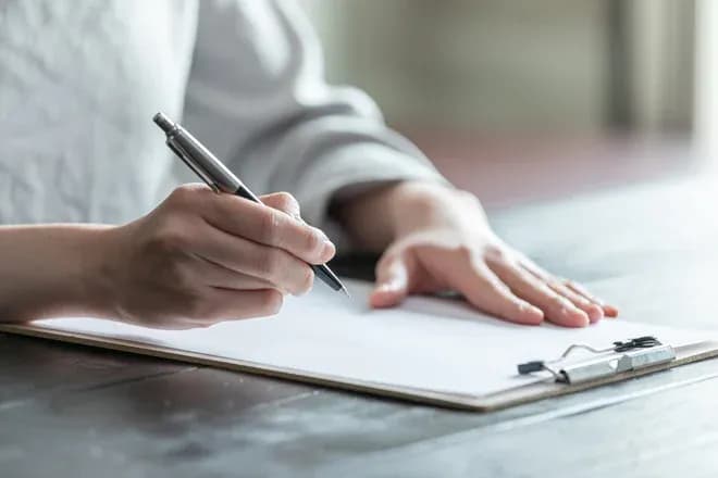 mains rédigeant un document sur une planchette à pince