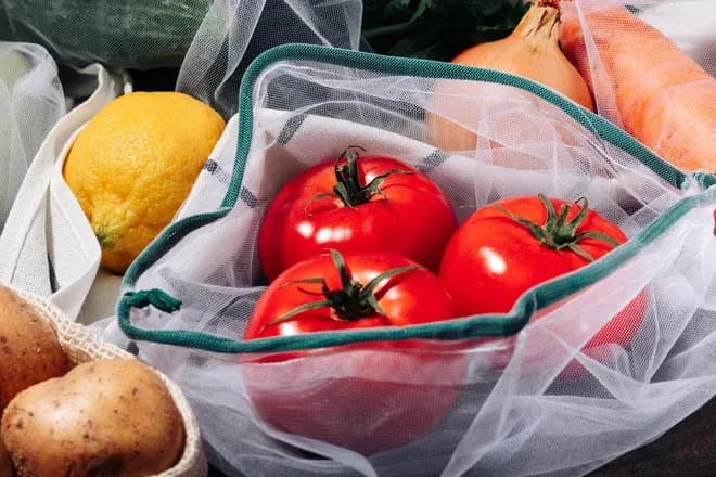 Tomates dans un sac réutilisable en filet entourées de pommes de terre citron oignon et carottes