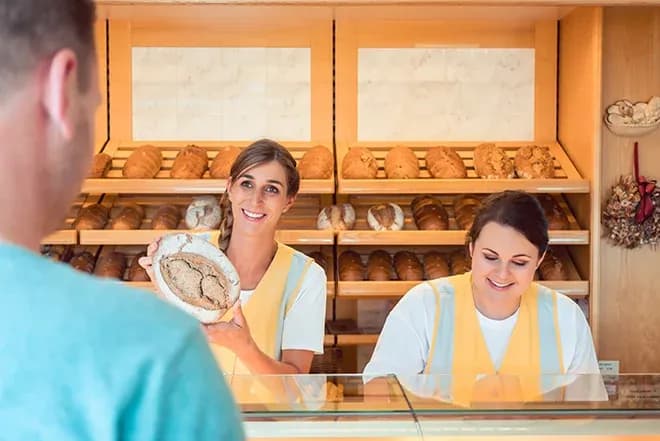 vendeuses souriantes présentant un pain dans une boulangerie avec des pains en arrière-plan