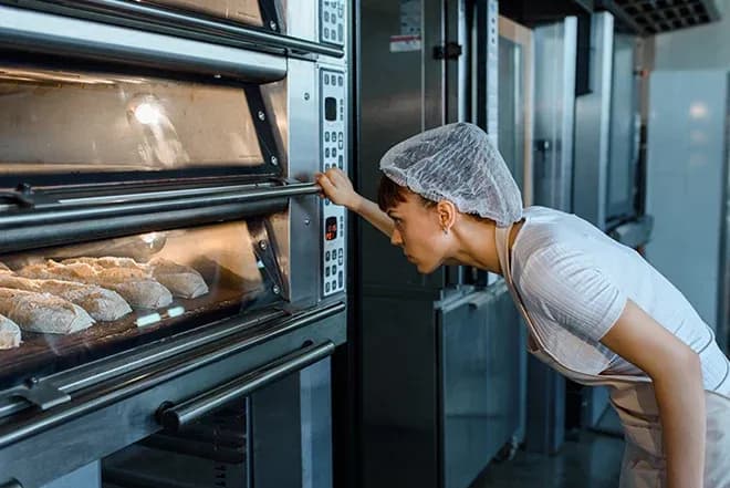 femme en charlotte vérifiant des pains dans un four professionnel