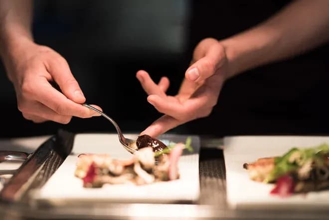 mains d'un chef dressant un plat gastronomique sur assiette blanche
