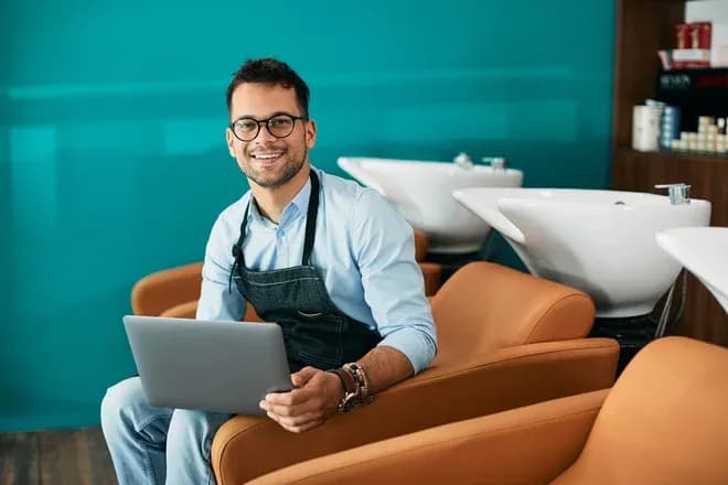 homme souriant avec un ordinateur portable dans un salon de coiffure moderne