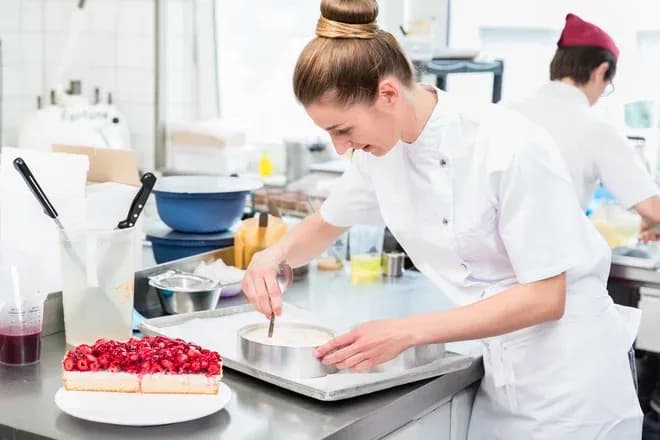 pâtissière en blouse blanche décorant un gâteau près d'une tarte aux fruits rouges