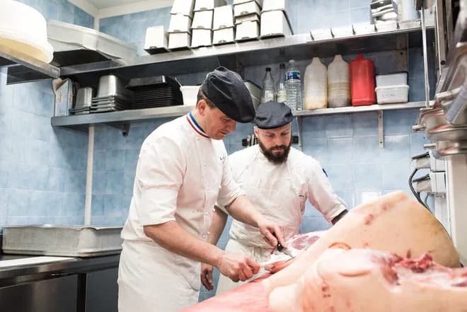 deux charcutiers en formation découpant une carcasse de porc dans une cuisine professionnelle