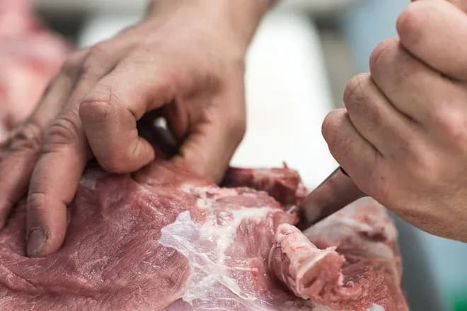 main en train de préparer de la viande avec un couteau dans un environnement de travail