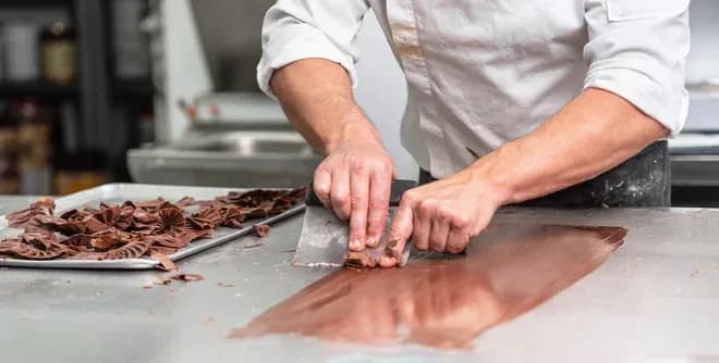 mains d'un chocolatier qui tempère et façonne du chocolat sur plan de travail