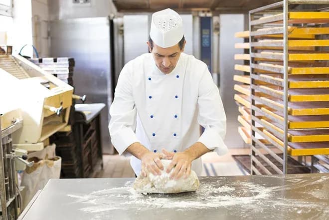boulanger pétrissant de la pâte sur un plan de travail dans une boulangerie