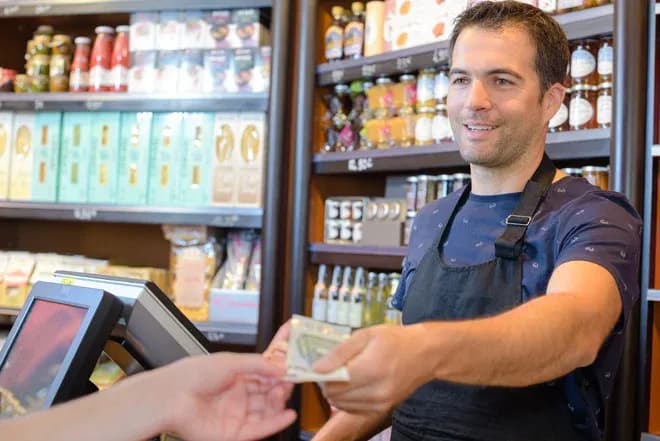 épicier souriant tendant des billets au client au comptoir