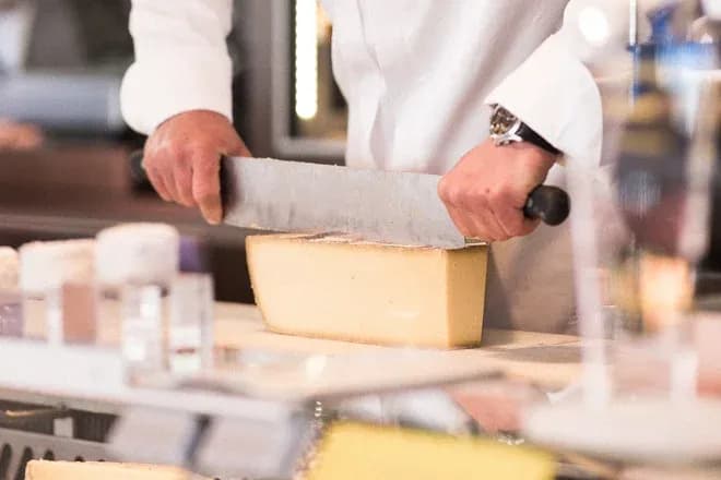 fromager en blouse coupant un bloc de fromage avec un grand couteau