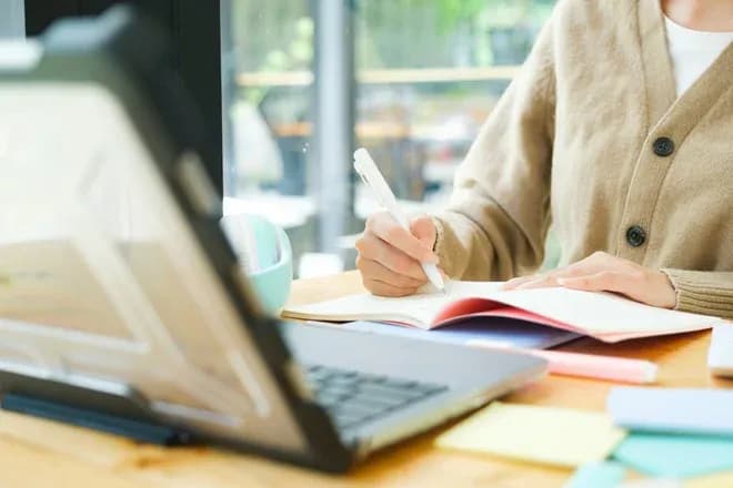 personne prenant des notes sur un carnet avec un ordinateur portable et des fournitures de bureau