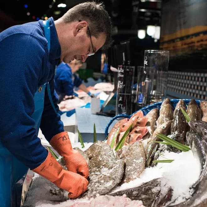poissonnier avec gants orange dispose des poissons sur glace