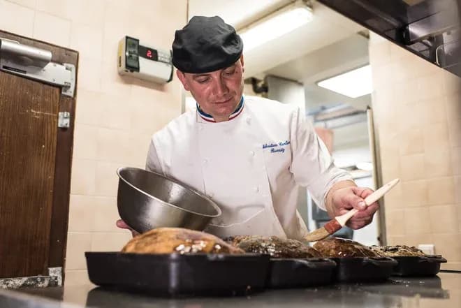Chef en train de badigeonner des plats dans une cuisine professionnelle avec des ustensiles de cuisine