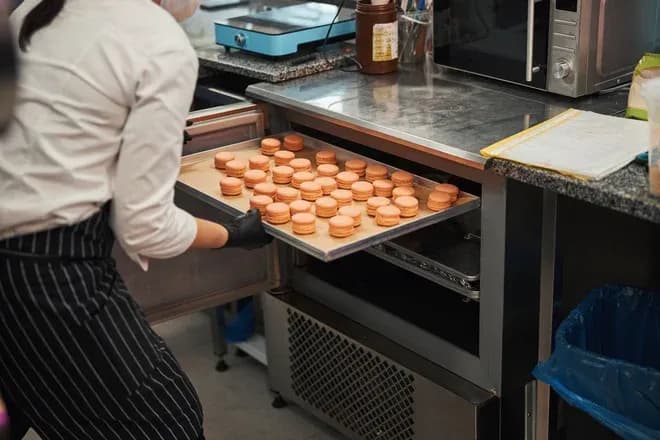 pâtissier retirant un plateau de macarons roses du four