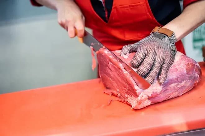 boucher découpe une pièce de viande avec un gant en mailles