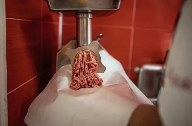viande hachée s'écoulant d'un hachoir en inox sur du papier