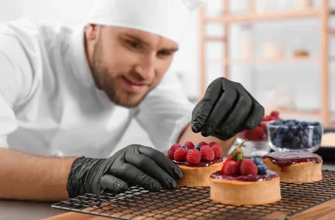 pâtissier en gants noirs disposant des framboises sur tartelettes