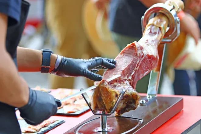 personne en gants coupant des tranches fines de jambon sur un support
