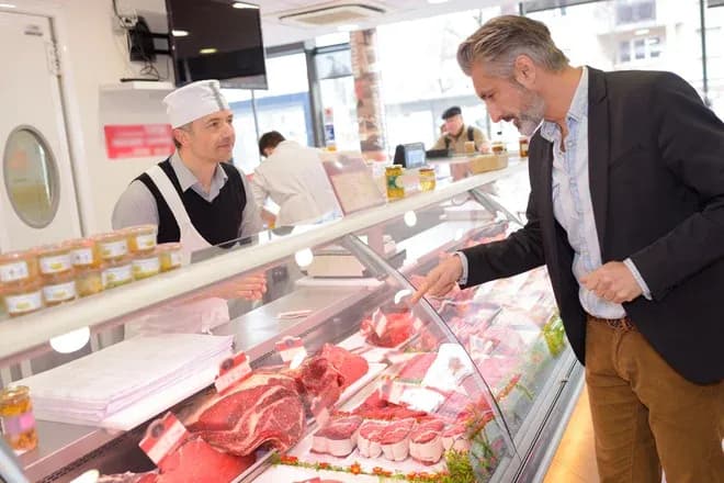 client observant des viandes dans une boucherie avec un boucher en arrière-plan