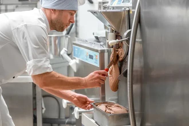 chef en blouse recueillant glace au chocolat d'une machine professionnelle