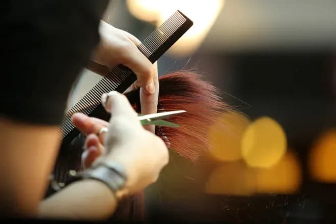 mains d'un coiffeur coupant une mèche auburn avec peigne et ciseaux