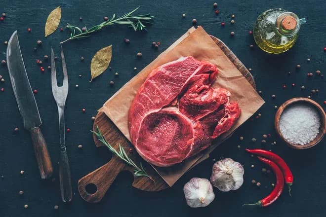 viande rouge crue sur une planche en bois avec des herbes épices et de l'huile d'olive