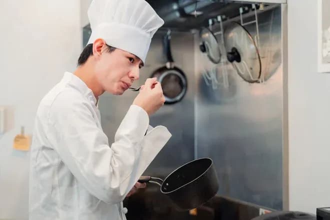 jeune chef goûtant une préparation dans une cuisine professionnelle