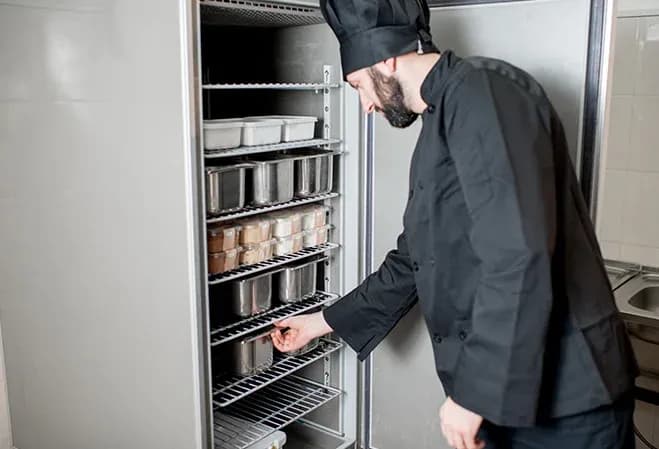 chef en uniforme vérifiant des contenants dans un congélateur professionnel