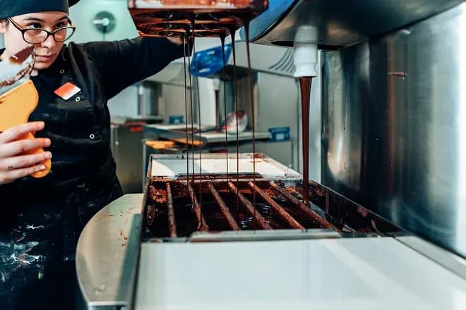 femme versant du chocolat fondu dans un équipement de pâtisserie professionnel