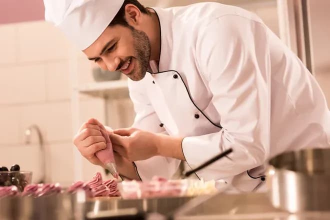 pâtissier souriant en train de décorer des desserts avec une poche à douille