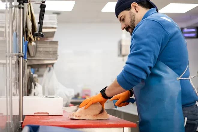 Homme en tablier découpant un poisson sur une table de travail en milieu professionnel