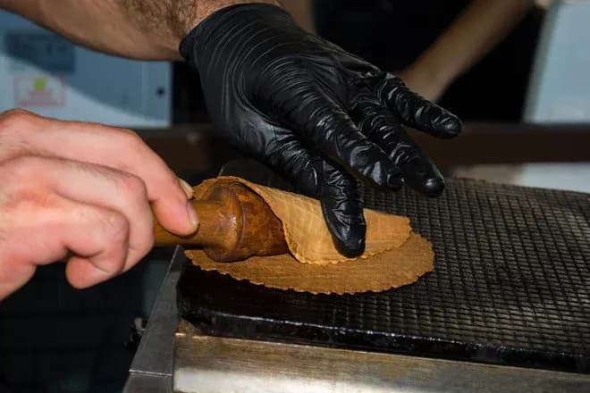 Préparation d'une gaufre enroulée sur un moule avec des gants noirs sur une plaque chaude