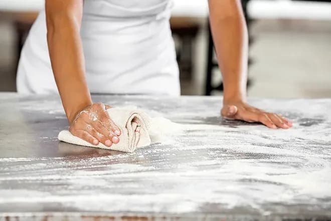 mains essuyant de la farine sur un plan de travail avec un torchon