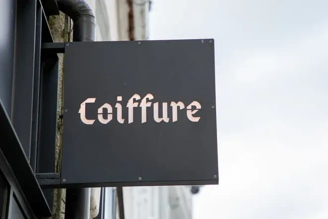 enseigne noire portant le texte coiffure suspendue devant une façade de salon