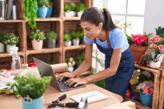 Fleuriste en tablier consulte un ordinateur portable dans son atelier fleuri