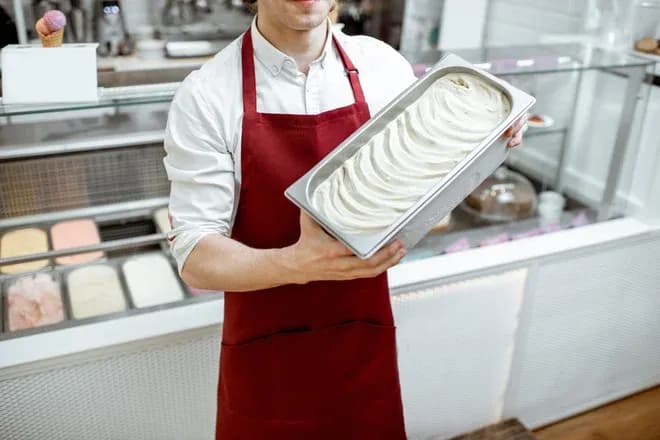 glacier en tablier rouge tenant un bac de glace vanille devant le comptoir