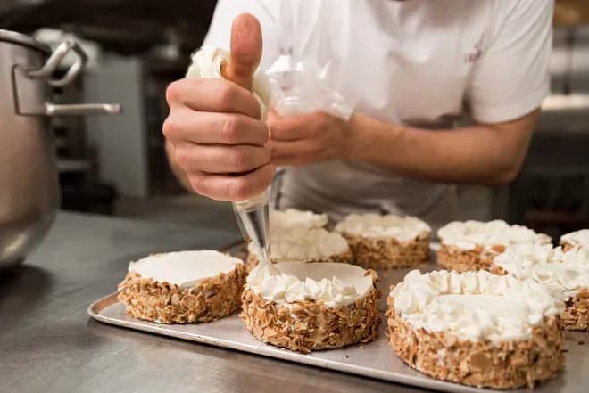 pâtissier décorant des gâteaux avec de la crème sur une plaque en cuisine professionnelle