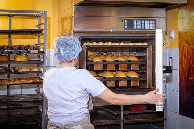 boulanger sortant des pains dorés d'un four dans une boulangerie professionnelle