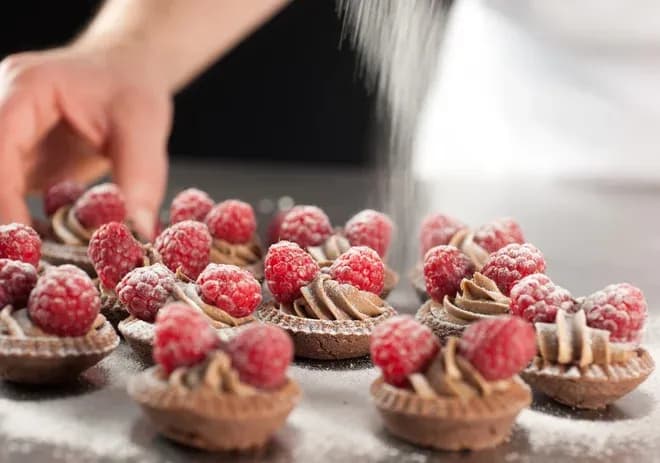 tartelettes au chocolat garnies de crème et framboises saupoudrées de sucre glace